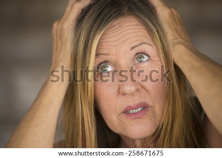 Portrait attractive mature woman, stressed, anxious, scared, unhappy expression, hands covering head, upward look, blurred background.