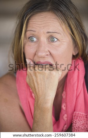 Portrait scared mature woman, fearful, shocked stressed, worried facial expression, nail biting, hand between teeth, blurred background.