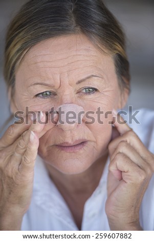 Portrait attractive mature woman stressed in pain with band aid on nose and unhappy facial expression, blurred background.