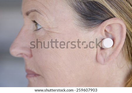 Profile Portrait attractive senior woman blocking sound with ear plug.