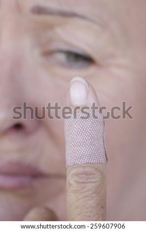 Injured Finger with protective band aid, sad female face in blurred background.