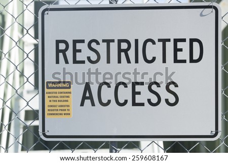 Restricted Access Sign at fence of property building, warning of asbestos material, health risk and hazard, blurred background.