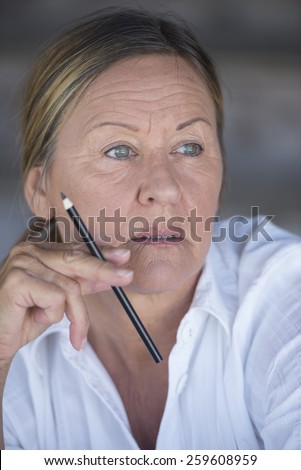 Portrait confident creative attractive mature business woman, thoughtful, serious, worried, with pen in hand, blurred background.