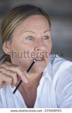 Portrait confident creative attractive mature business woman, thoughtful, serious, with pen in hand at lips, blurred background.