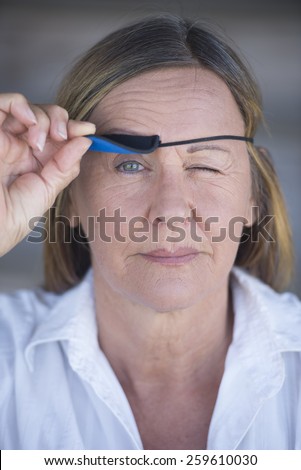 Portrait confident attractive mature woman lifting eye patch worn as protection after injury, blurred background.