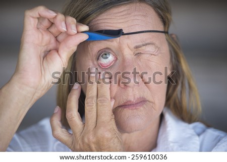 Portrait suffering attractive mature woman lifting eye patch worn as protection after injury, blurred background.
