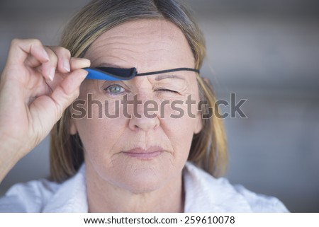 Portrait confident relaxed attractive mature woman lifting eye patch worn as protection after injury, blurred background.