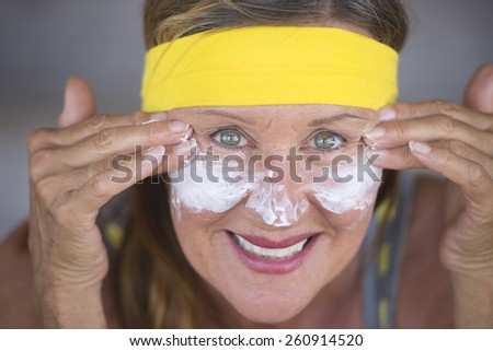 Portrait sporty fit attractive mature woman with protective sunscreen skin care creme and moisturiser lotion on happy smiling face, yellow headband, blurred background.