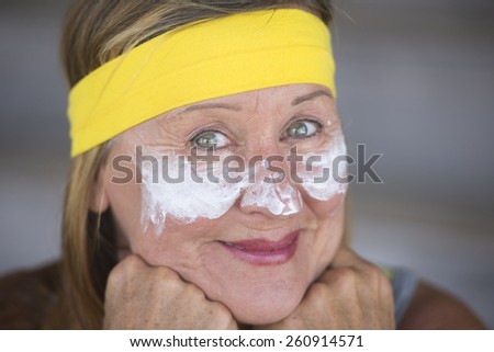Portrait fit active attractive mature woman with protective sunscreen skin care creme and moisturiser lotion on happy smiling face, yellow headband, blurred background.