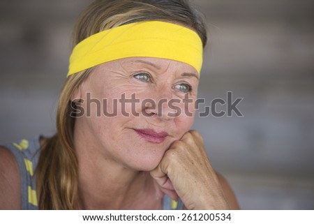 Portrait active sporty attractive mature woman, confident happy relaxed smiling after healthy exercising, yellow headband, blurred background.