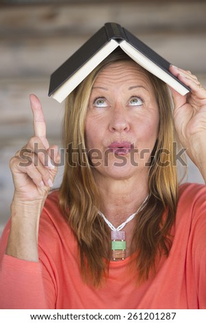 Portrait attractive mature woman with book on head, happy smart look, waiting for inspiration and idea, blurred background, copy space.