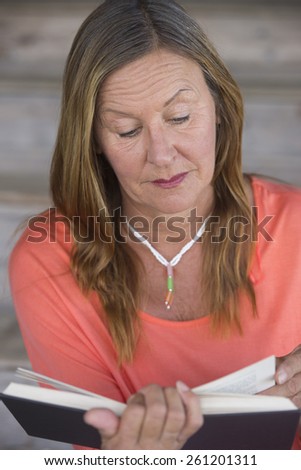 Portrait attractive mature woman reading a book for relaxing entertainment, learning, inspiration, blurred background.