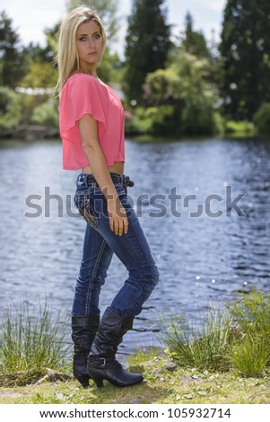 Young woman outside in the park by the lake wearing jeans and boots