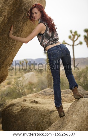 Young model posing outdoors by a rock in a desert landscape