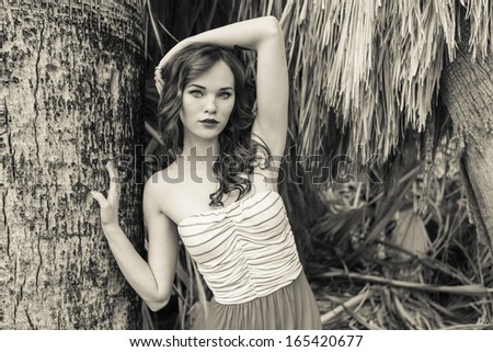 Black and white photo of a young model posing next to a palm tree