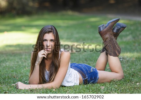 Long hair brunette posing and laying on the grass outdoors wearing boots