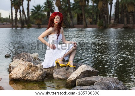 Redhead model posing on a rock by a dress with palm trees