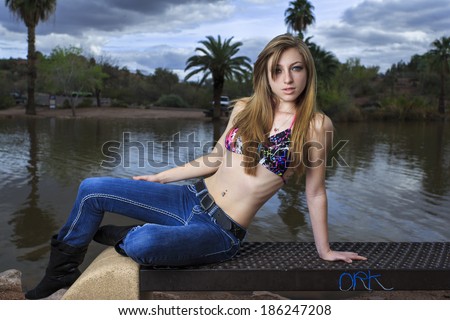 Sexy model posing in bikini top and jeans at sunset