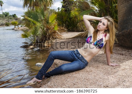 Gorgeous model posing by the water in low rise jeans and bikini top