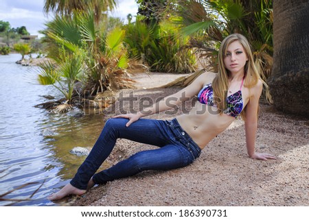 Beautiful blond model posing in jeans and bikini top on a beach