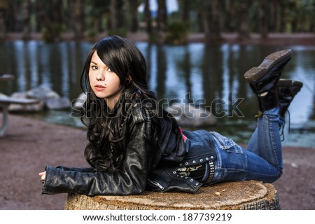 Portrait of a jet black hair teen in black leather jacket posing on a tree trunk