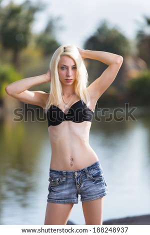 Young blonde and skinny model with straight hair posing in swimwear and jeans shorts