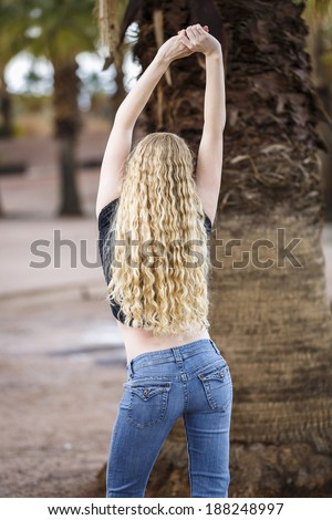 Young lady with long curly hair and tight jeans with arms up
