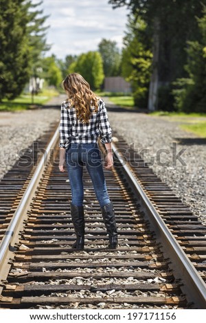 young girl walking on the train tracks in flannel shirt and jeans