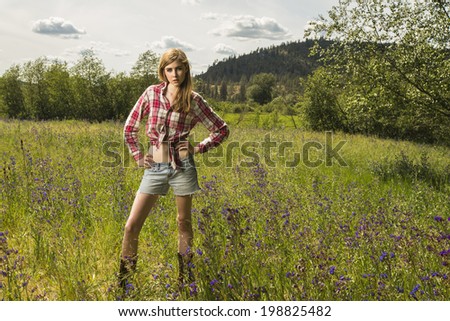 Beautiful and young girl posing outdoors in the grassy field in red flannel shirt and jeans shorts