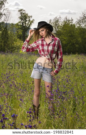 Young female model in tied up flannel shirt and wearing cowboy hat
