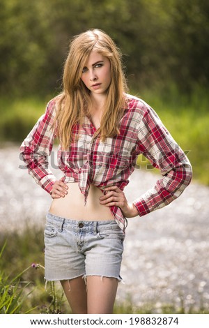 Young western teenage girl in tied flannel shirt and denim shorts