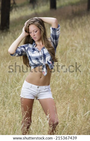 beautiful and young country girl posing outdoors in white shorts and flannel shirt