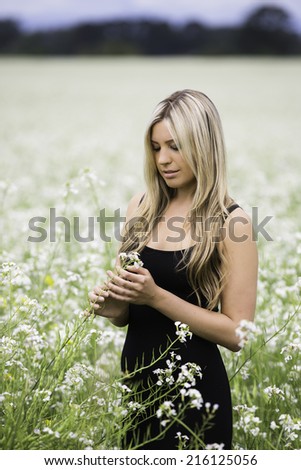Lifestyle portrait of a young blond model looking at a natural flower