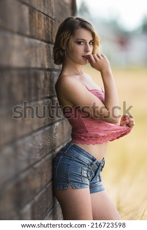 Sassy and shy young girl posing and leaning against a wooden wall
