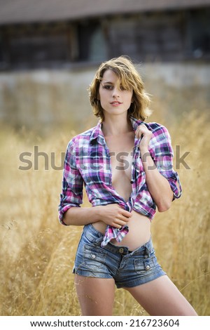 Young attractive woman wearing tied up flannel shirt and jeans shorts posing outdoors