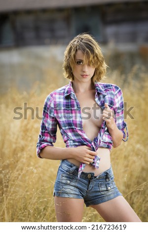 Sassy young lady posing with untied shirt and denim pants with grassy field background