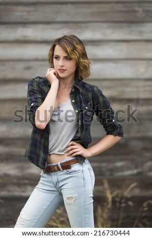 Young female girl with one arm up next to her face posing next to a wooden background