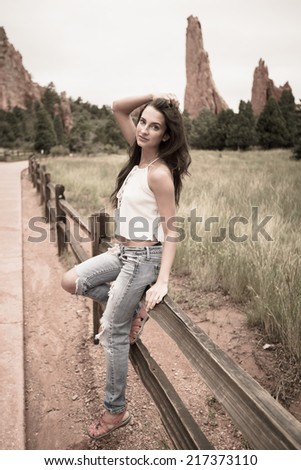 Young woman posing and sitting on a fence outdoors in a park with rock spires