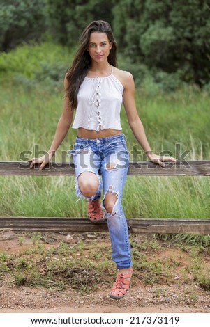 Young female brunette model with straight long hair posing and sitting on a fence outdoors