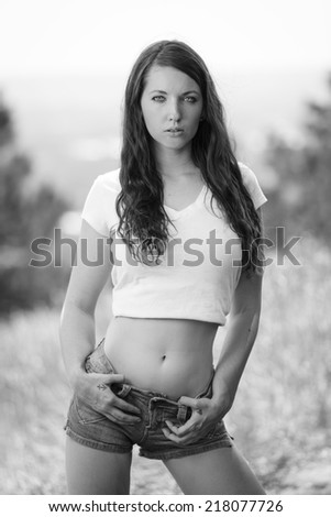 Black and white portrait of a young woman posing in low rise jeans shorts