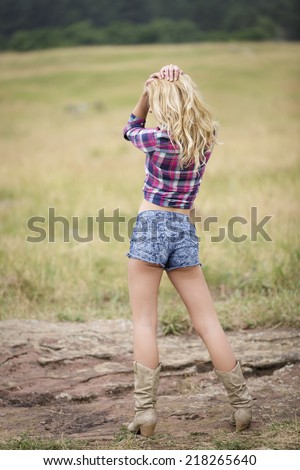 Portrait of a curly blond girl posing from behind in denim shorts and red flannel shirt