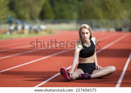 Young fit girl sitting on the track and stretching and determine