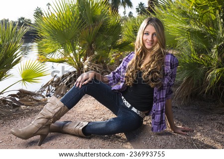 Young girl with tall boots and purple flannel shirt posing on the ground in a tropical environment