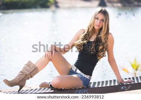 Sassy young blond girl posing in denim shorts and tall boots outdoors