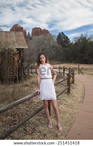 Young brunette girl in a white dress posing in rustic park