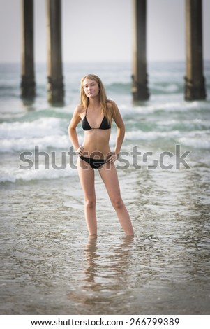 Full body portrait of a young blond woman posing in the water wearing black bikini swimwear