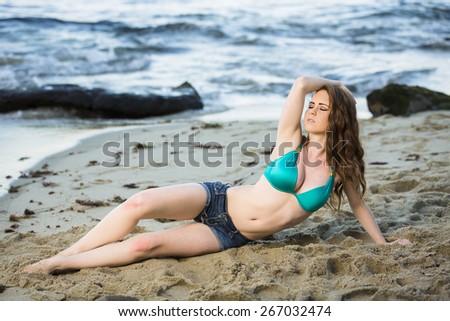 Sassy young attractive girl laying on the beach in jeans shorts and bikini top