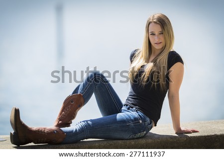 Young blonde girl posing in cowboy boots an laying on the ground outdoors