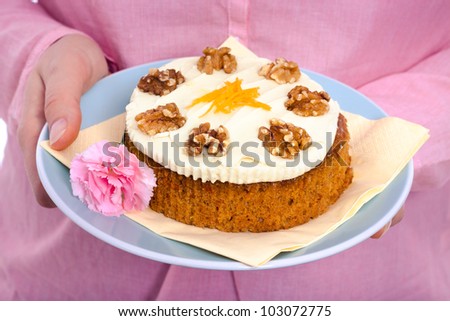 Delicious whole carrot cake with icing, grated carrots and walnuts on pink background.