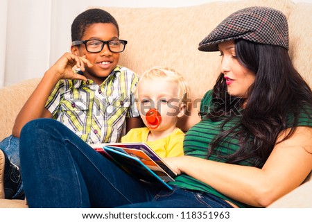Young happy woman with children reading book and relaxing on sofa.